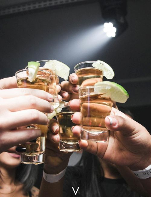 A group of friends clinking shot glasses with lime wedges at a party, cheers to a toast.