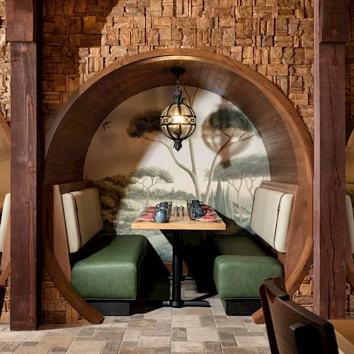 A cozy caf&eacute; booth with green cushioned seats under a wooden arch, lantern lights, and a painted nature mural on the wall.