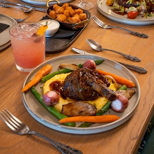 A restaurant table set with roast meats, sides, salad, snacks, and drinks&mdash;wine and pink lemonade&mdash;ready to eat.