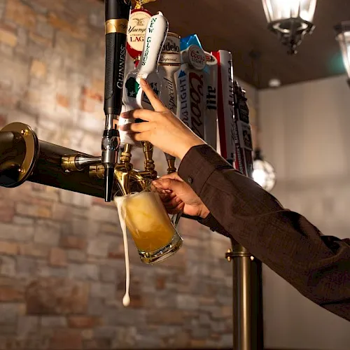 A bartender pours a fresh beer from the taps, with hands adjusting the bar line in a cozy, warmly lit pub.