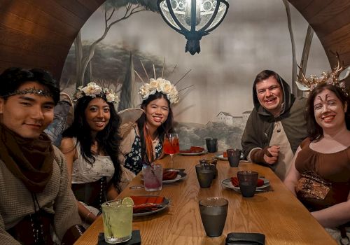 A group of five friends in festive winter outfits and antlers sit at a table with drinks and food, smiling for a photo.